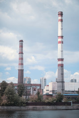 factory pipes in the city pollute the air near the water and trees in the summer