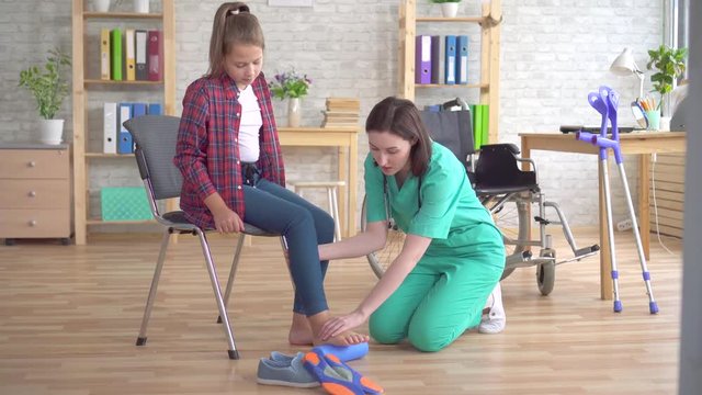 doctor helps in rehabilitation to stretch the leg with the help of a roller of a teenage girl in a wheelchair