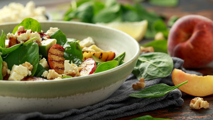 Summer Peach Salad with spinach, avocado, walnuts and feta cheese in rustic bowl. healthy food.