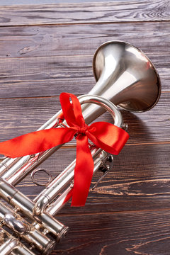 Silver trumpet with red ribbon. Shiny musical instrument with red bow on wooden table. Idea for gift.
