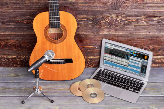 Musical equipment on wooden background. Acoustic guitar, microphone, laptop and cd disks on wooden background.