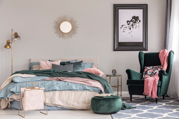 Emerald green armchair with floral pillow and pastel pink blanket in trendy bedroom interior