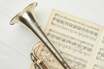Old trumpet on musical notes close up. Musical notes book and trumpet. Antique instrument of jazz music.