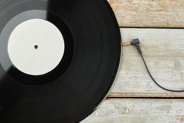 Vinyl LP record on wooden background. Vinyl disc and cable from earphones on wooden surface. Audio...