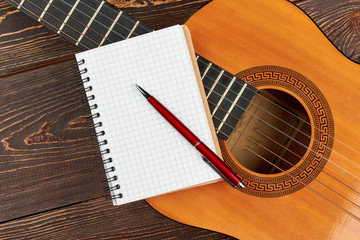 Fototapeta premium Blank notebook and pen on guitar. Acoustic guitar with notebook and pen on wood background.