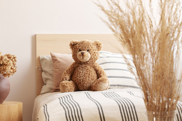 Brown cute teddy bear on single wooden bed with striped bedding