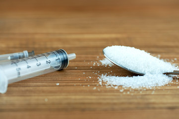 spoon with sugar and syringe on wooden background