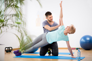 Middle age woman exercising on blue mat during physiotherapy with young male doctor