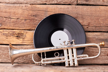 Trumpet and plastic record on wooden background. Classical jazzy instrument. Black vinyl LP record.