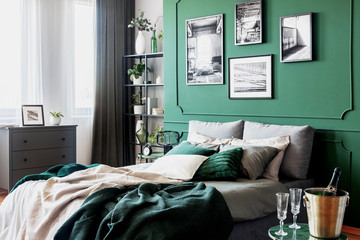 Gallery of black and white poster on green wall behind king size bed with pillows and blanket