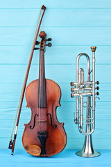 Naklejka premium Musical instruments of orchestra. Brown violin, bow and trumpet on blue wooden background, vertical image. Classical orchestral equipment.