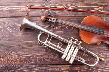 Vintage equipment of orchestra music. Violin, fiddle stick and trumpet on brown textured wood.