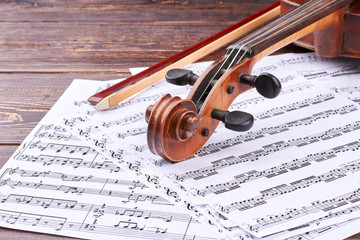 Naklejka premium Violin scroll and peg box on musical notes. Music note sheets, violin and fiddle stick on wooden background. Detail of violin. Classical music concept.