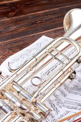 Trumpet and musical notes, vertical image. Music note sheets and trumpet on wooden background. Classical music equipment.