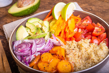 Salad bowl with quinoa; carrots; avocado; onion; pepper; tomato with slices of lime close-up - vegetarian dish; buddha bowl