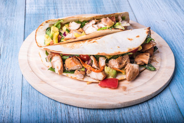 Tacos with vegetables, avocado and chicken breast on a wooden round board - traditional mexican appetizer