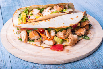 Tacos with vegetables, avocado and chicken breast on a wooden round board closeup - traditional mexican appetizer