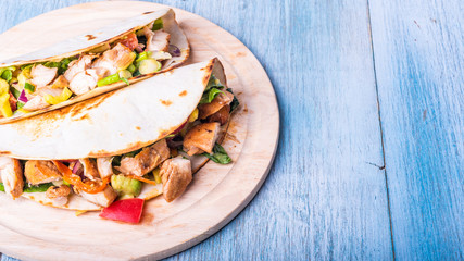 Tacos with vegetables, avocado and chicken breast on a wooden round board - traditional mexican appetizer