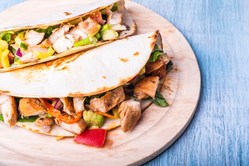 Tacos with vegetables, avocado and chicken breast on a wooden round board closeup - traditional mexican appetizer