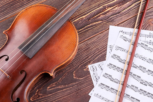 Violin and musical notes on wooden background. Brown vintage violin, bow and musical notes on brown wooden table close up. Classical music background.