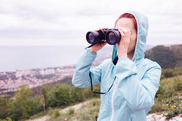 Traveler young woman looking through binoculars in summer outdoor.