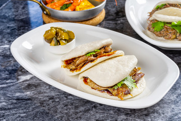 Close up view on bao with duck fillet. Gua bao, steamed buns served on white plate. Taiwan's traditional food Gua Bao on marble table. Asian sandwich steamed. Asian fast food. Meat