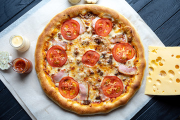 Delicious homemade pizza with ingridients on dark background top view. Flat lay pizza with ham, tomato and melted cheese. Viw from above traditional italian cuisine. Food for lunch