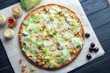 Delicious homemade pizza with ingridients on dark background top view. Flat lay pizza with chickeni, lettuce, crackers and melted cheese. Viw from above traditional italian cuisine. Food for lunch