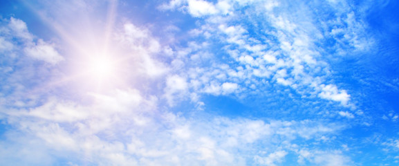 Naklejka na ściany i meble Bright sun on blue sky with white clouds. Wide photo.