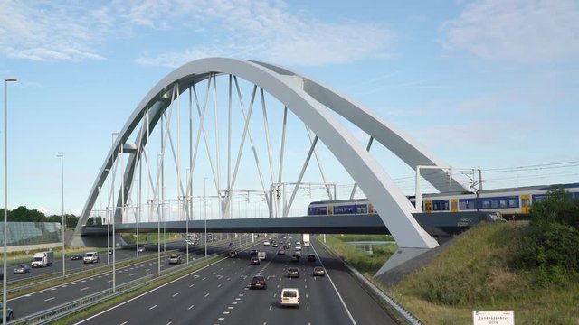 Sprinter trains passing each other on the train bridge to Almere to Amsterdam crossing Commuters in cars driving on highway A1, Muiden, The Netherlands, July 9th 2019