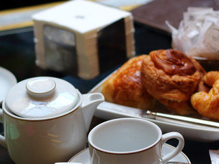 Taza de café, jarra con leche, croissants y servilletas sobre una mesa listo para el desayuno o la merienda.