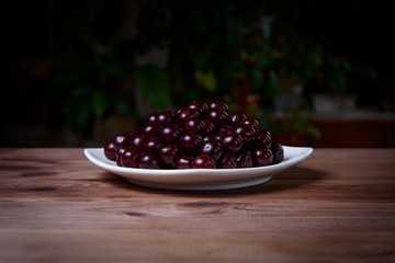 Cherry on a white plate on a wooden table.