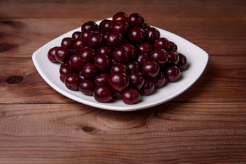 Cherry on a white plate on a wooden table.