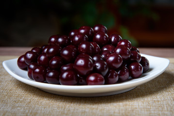 Cherry on a white plate on a wooden table.