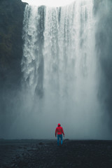 Obraz premium Skogafoss waterfall Iceland. Man standing against huge waterfall surrounded by green hills. Spring in Iceland.