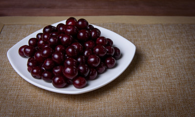 Cherry on a white plate on a wooden table.