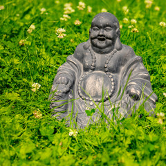 Figure of a Buddha sitting in the garden amid blooming clover.