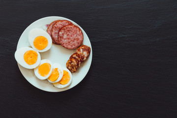 Breakfast plate made of sausage, egg and salami slices – Appetizer meal rich in fat and proteins on dark textures stone background with copy space
