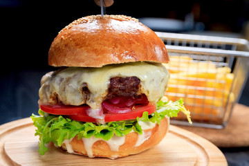 American fast food. Juicy American cheeseburger with beef cutlets, sauce and tomato on a black background.