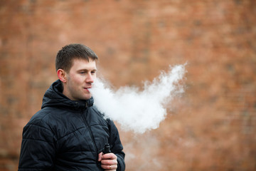 Vape man. Young caucasian white guy in black jacket smoking and letting off steam from an...
