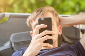 Junger Mann mit Handy in der Hand liegt lässig auf einer Liege im Garten