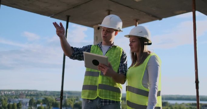 Construction worker man and architect woman in a helmet, discuss the plan of construction of house, tell each other about the design, holding a tablet, look at the drawings, background of sun rays