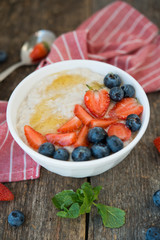 Healthy Breakfast oatmeal bowl with berries and honey on rustic wooden background