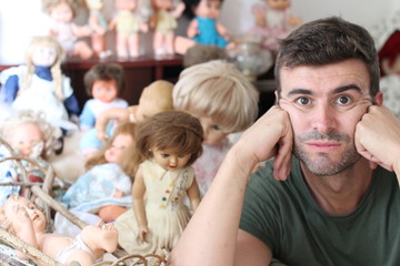 Bored man with lots of dolls in the background 