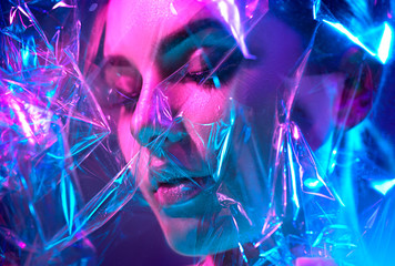 Fashion model woman in colorful bright neon lights posing in studio through transparent film....