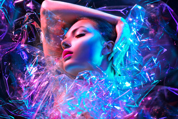 Femme mannequin dans des néons lumineux colorés posant en studio à travers un film transparent. Portrait de belle fille sexy en UV. Maquillage coloré de conception d& 39 art