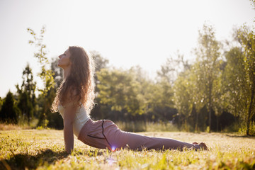 Young woman in yoga clothes is practising yoga in the open air in the nature on the grass on the sunny day