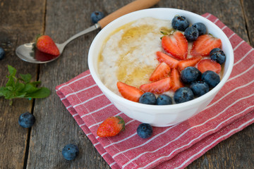 Healthy Breakfast oatmeal bowl with berries and honey on rustic wooden background