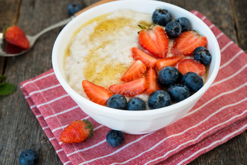 Healthy Breakfast oatmeal bowl with berries and honey on rustic wooden background