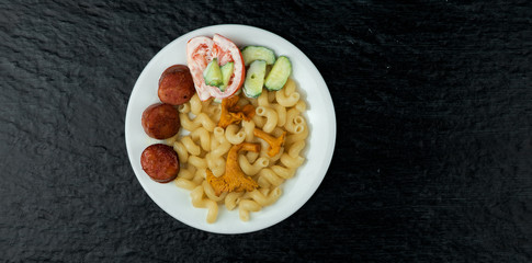 FOOD IN POT. PASTA, SALAD AND FOX MUSHROOMS IN THE WHITE CERAMIC PLATE ON A DARK BACKGROUND. VIEW FROM ABOVE. COPY SPACE